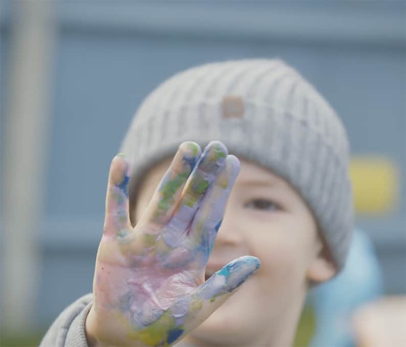 A small child with a woolley hat on is holding his hand to the camera. It is covered in paint. By video production company Vermillion Films in Birmingham and London