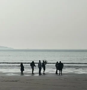 Video Production features a silhouetted film crew at the beach. 6 people standing around a camera man