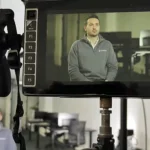 Still image from behind the scenes of filming a startup video. Shows a monitor with a guy being interviewed in an office.