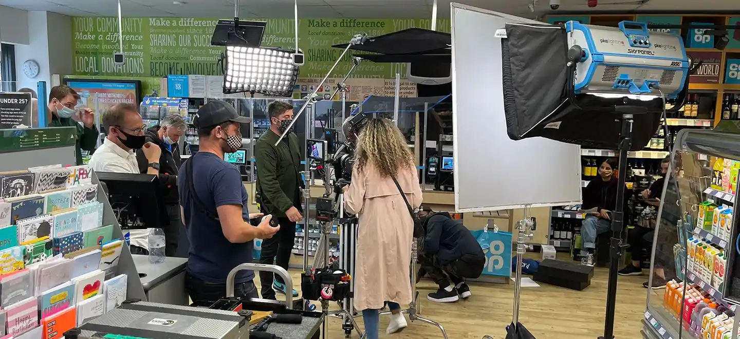 Photo shows a TV commercial production. There are various people in a co-op store surrounded by filmmaking equipment