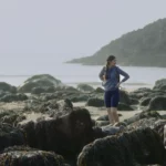 Brand video for startups still image shows a young woman with her hands on her hips looking around at a beautiful rocky beach in South West Wales