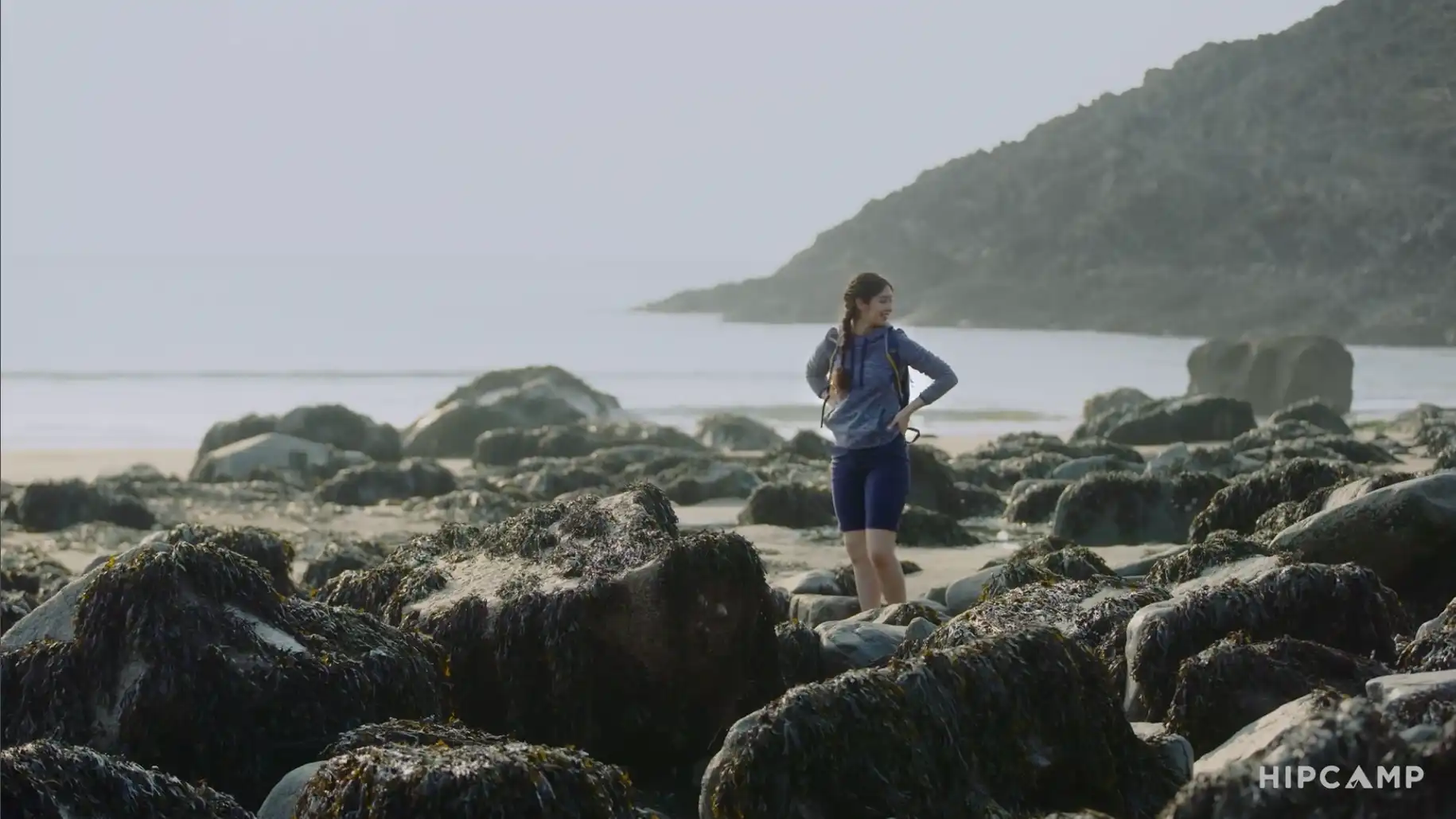 Brand video for startups still image shows a young woman with her hands on her hips looking around at a beautiful rocky beach in South West Wales