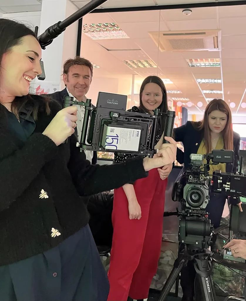 A group of people standing around a monitor looking really quite happy