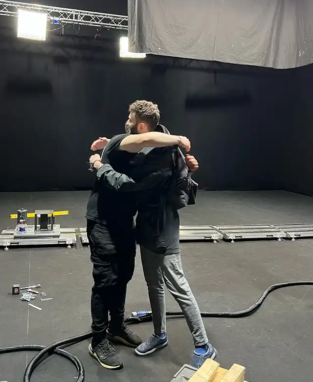 Two men hugging in a film studio amid a complex video production